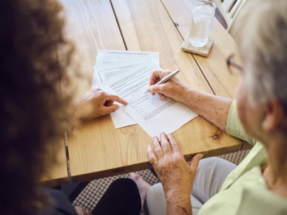 Young woman sits at a table with an older woman who is signing documents