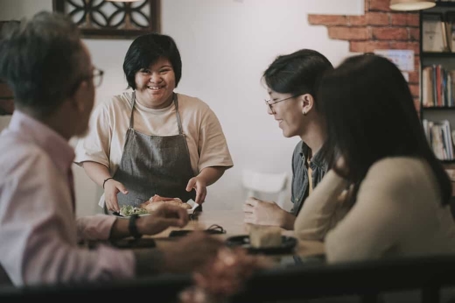 Restaurant worker with special needs serves plates of food to hungry customers seated at a table