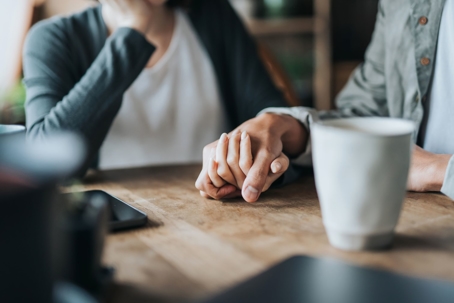 A couple holds hands on a table while drinking coffee