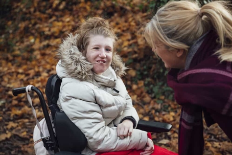 Teen girl with special needs in a wheelchair with a fluffy coat on during fall as her mother talks to her