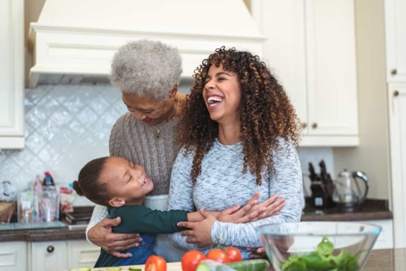 Grandmother, mother, and daughter laughing and hugging in the kitchen