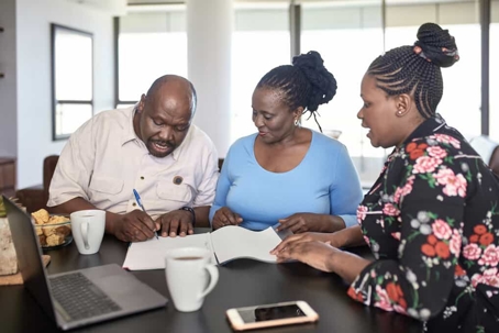 Young woman sits at a table with her parents as they sign a document