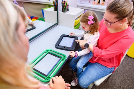 special needs child working on an ipad with a parent and teacher