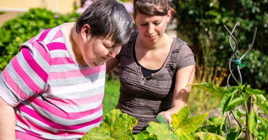 A woman and her special needs sister looking at a plant outside