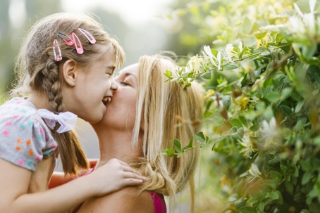 blonde woman holding and kissing her laughing daughter